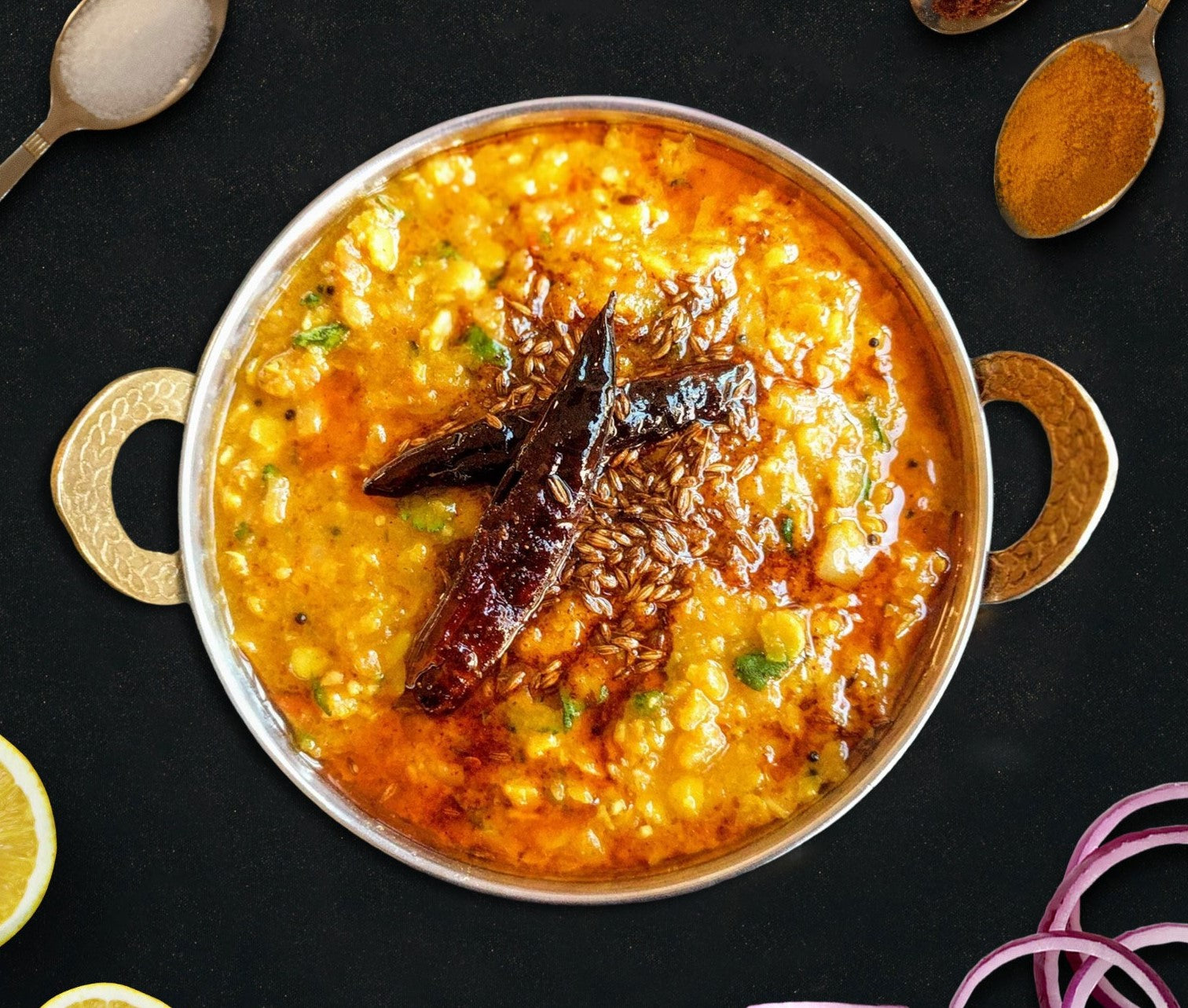 bowl of dal tadka with spices on a black background