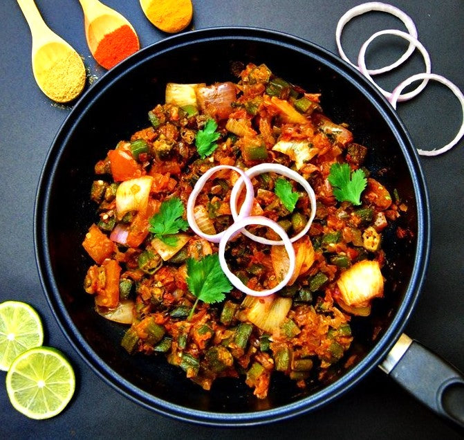 Bhindi Masala in a black pan with lime slices and spices on a dark surface