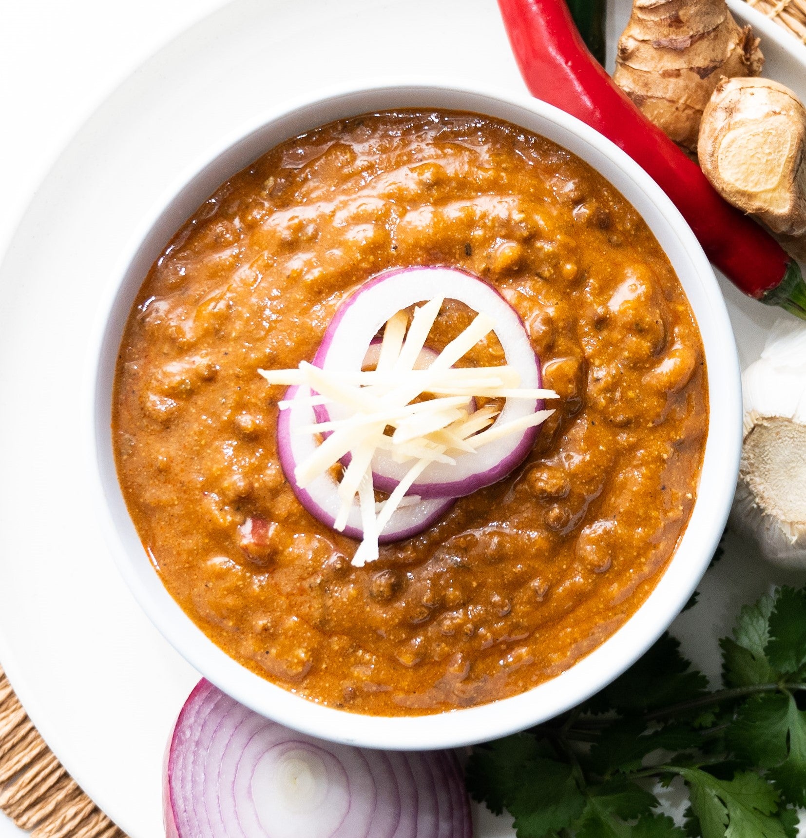 Red lentil soup in a white bowl with sliced onions on top, surrounded by ingredients.