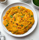 Stack of besan chilla on a white plate with green herbs, on a light gray surface.