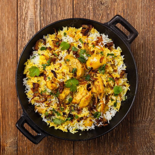 Black cast iron skillet with chicken biryani on a wooden surface